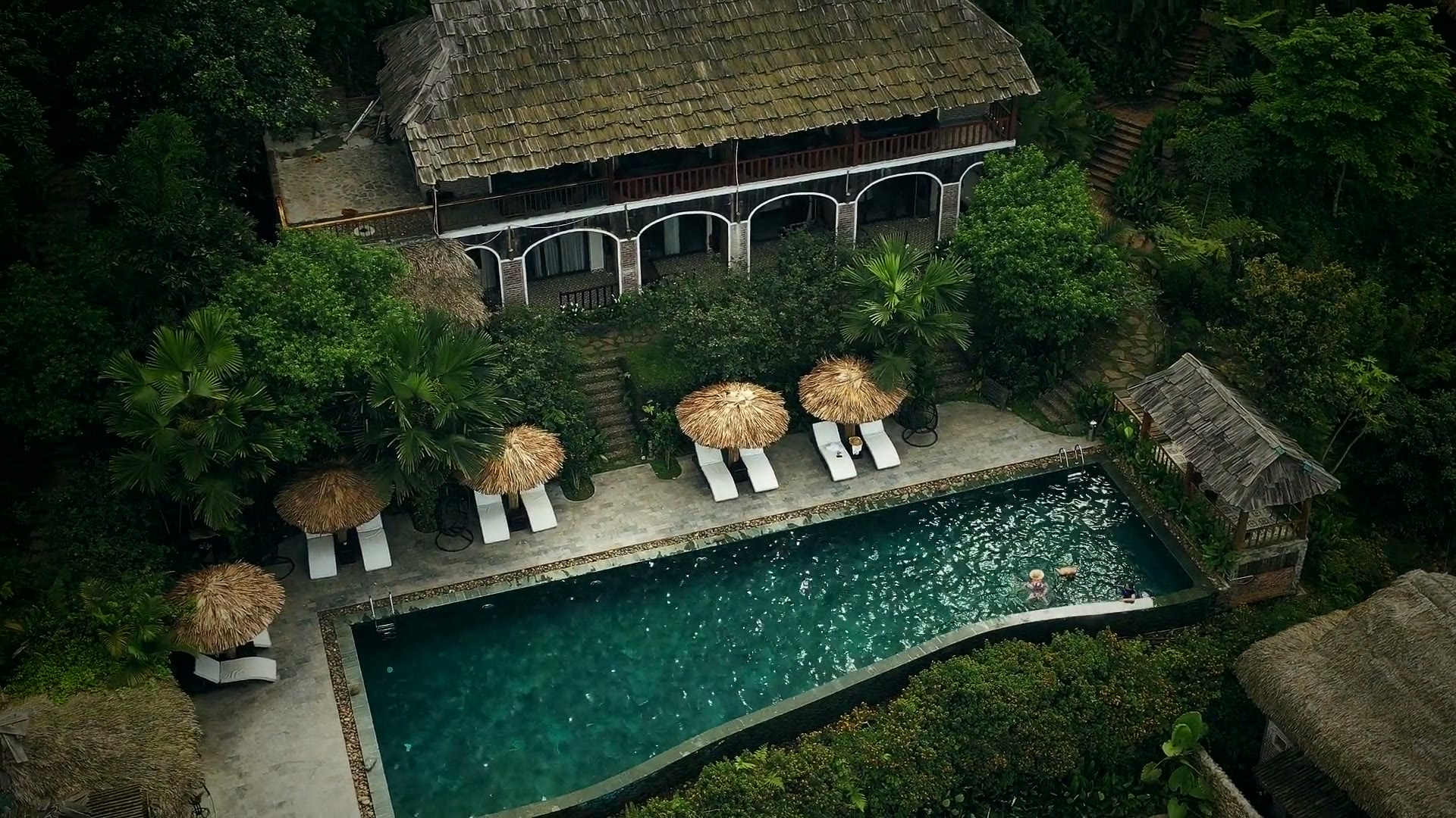 Thatched roofs and the long estate pool seen from above.